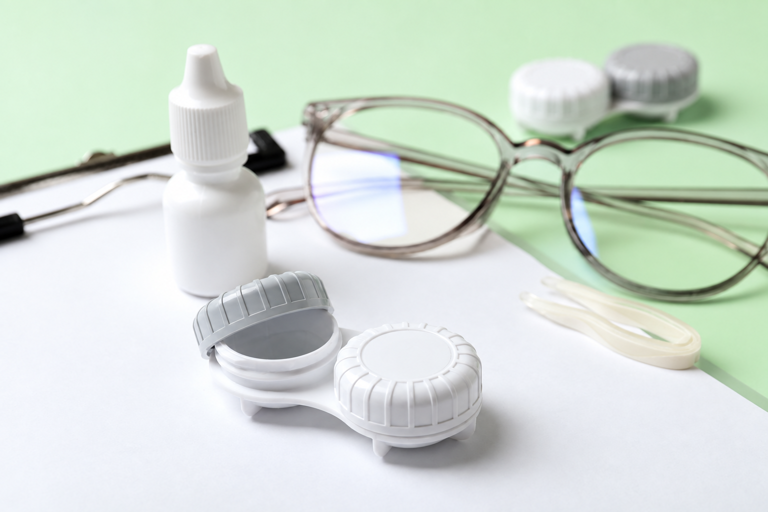 Gafas, gotas y estuches para lentes de contacto sobre un fondo verde menta